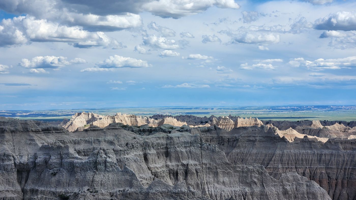 Layered Badlands formations with green prairie stretching to the horizon