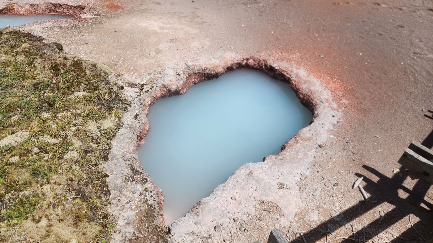 A small, impossibly blue hot spring pool rimmed in orange mineral crust