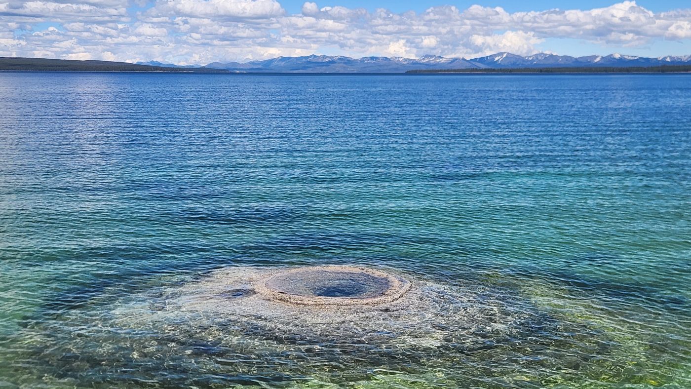 Fishing Cone, a geyser cone sitting out in the clear water of Yellowstone Lake with mountains beyond