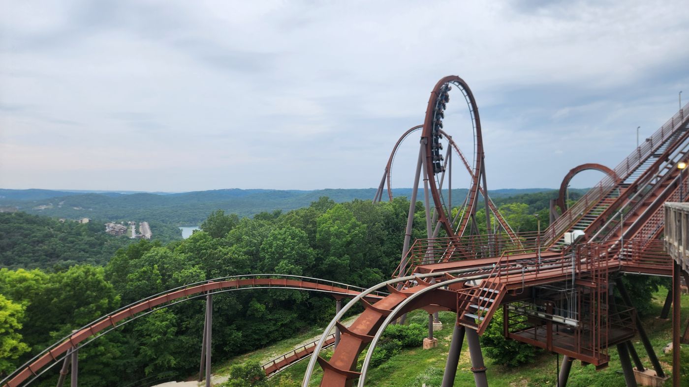 A roller coaster train mid-inversion above the green Ozark hills at Silver Dollar City